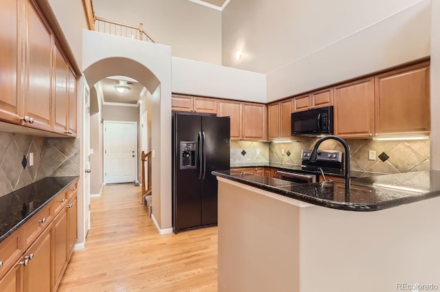 kitchen featuring decorative backsplash, dark stone countertops, black appliances, and light hardwood / wood-style floors