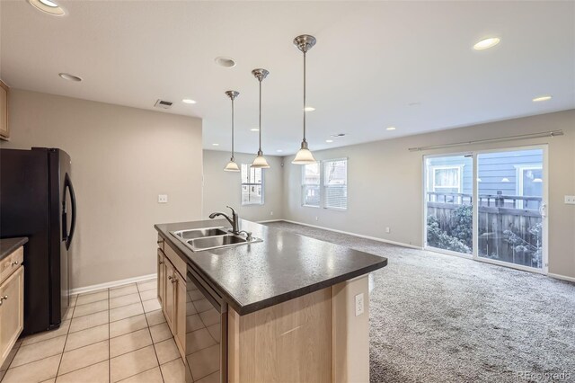 kitchen featuring sink, decorative light fixtures, dishwashing machine, black fridge, and a center island with sink