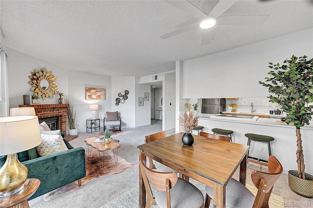 carpeted dining room with a textured ceiling, a fireplace, ceiling fan, and sink