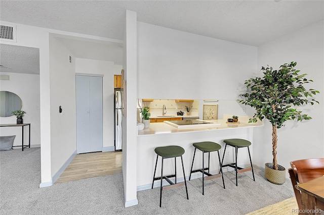 kitchen with a breakfast bar, light carpet, sink, kitchen peninsula, and stainless steel refrigerator