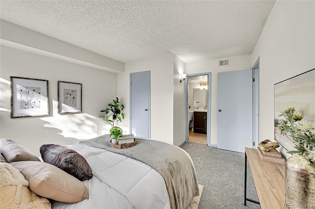 carpeted bedroom featuring a textured ceiling and ensuite bath