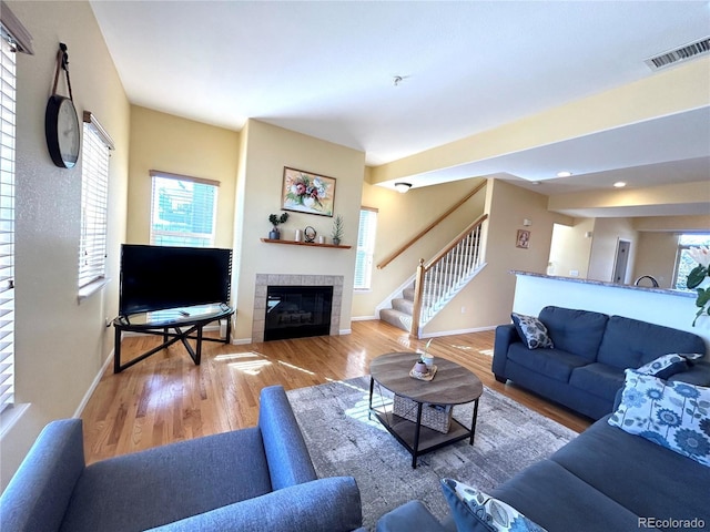 living room featuring a tiled fireplace, wood-type flooring, and a healthy amount of sunlight