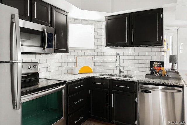 kitchen with backsplash, dark cabinets, light stone countertops, stainless steel appliances, and a sink