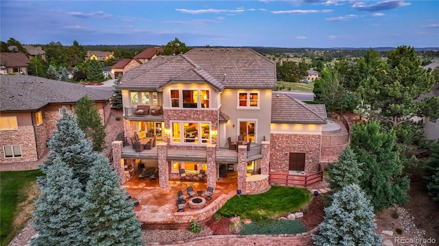 back house at dusk featuring a balcony and a patio