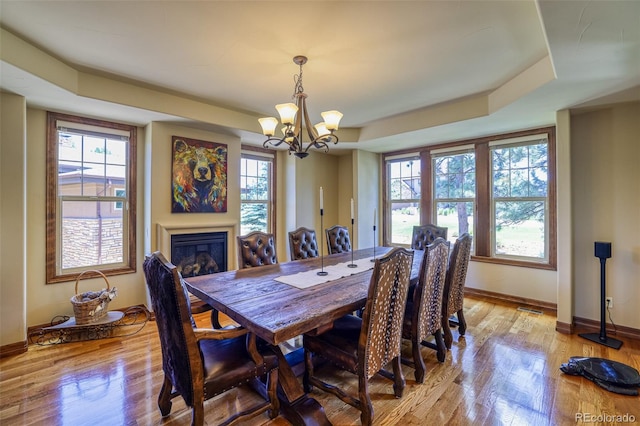 dining space with a notable chandelier, plenty of natural light, light hardwood / wood-style floors, and a tray ceiling