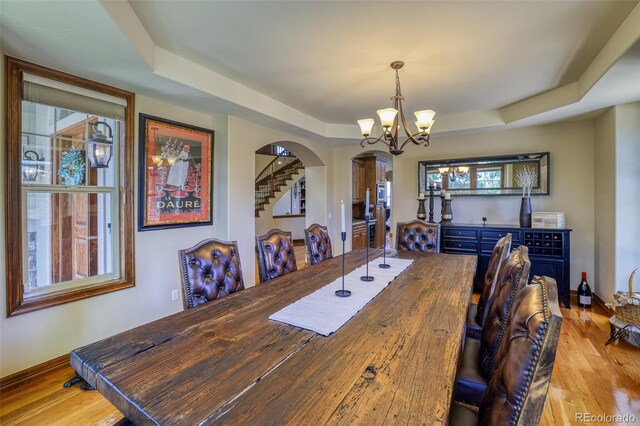 dining area featuring a tray ceiling, a chandelier, and light wood-type flooring