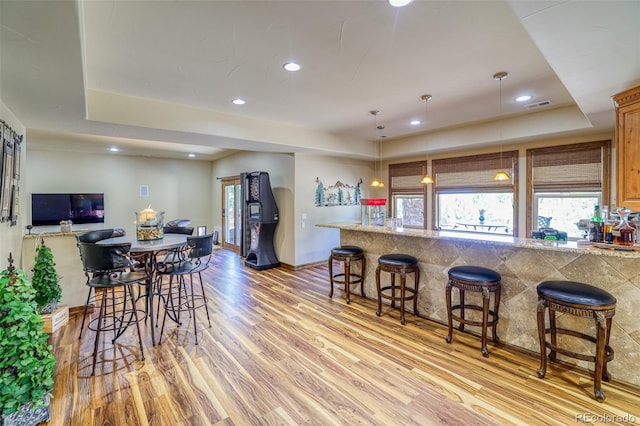 kitchen featuring a kitchen bar, pendant lighting, light hardwood / wood-style floors, and a raised ceiling