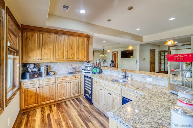 kitchen featuring sink, hanging light fixtures, wine cooler, light stone counters, and kitchen peninsula