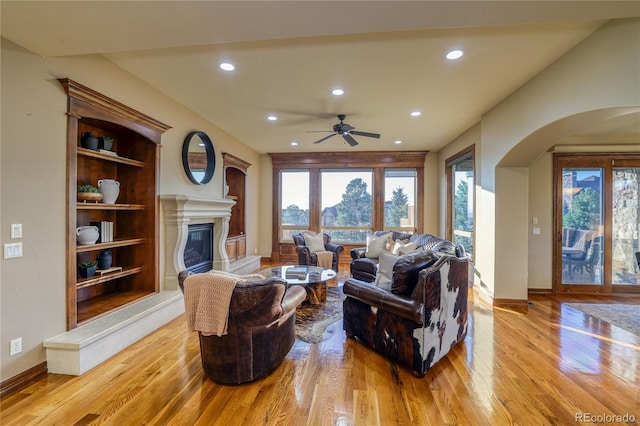 living room with built in shelves, light wood-type flooring, and ceiling fan