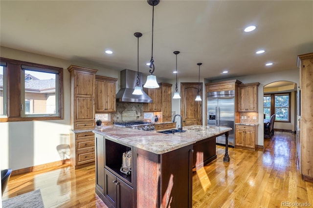 kitchen featuring hanging light fixtures, wall chimney range hood, backsplash, built in appliances, and a spacious island