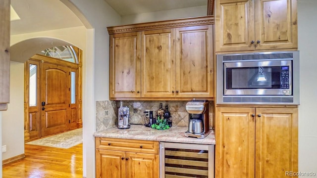 kitchen with decorative backsplash, light stone counters, light hardwood / wood-style flooring, wine cooler, and stainless steel microwave