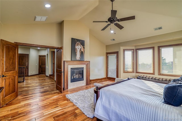 bedroom featuring light wood-type flooring, vaulted ceiling, ceiling fan, and a tiled fireplace