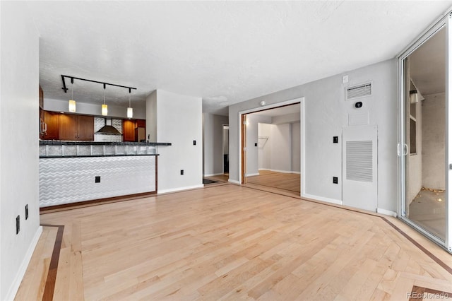 unfurnished living room with a textured ceiling, light hardwood / wood-style floors, and track lighting