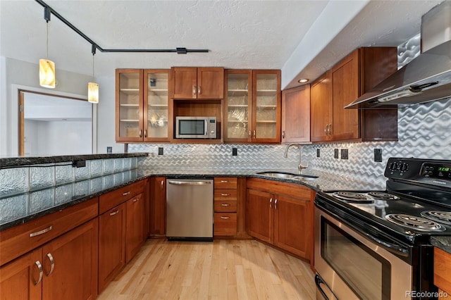 kitchen featuring appliances with stainless steel finishes, sink, dark stone countertops, and wall chimney range hood