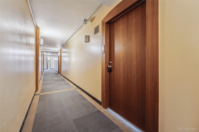 corridor with baseboards, visible vents, and light colored carpet