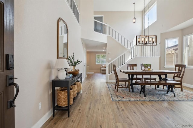 foyer entrance featuring a towering ceiling, light wood-type flooring, stairs, a chandelier, and baseboards