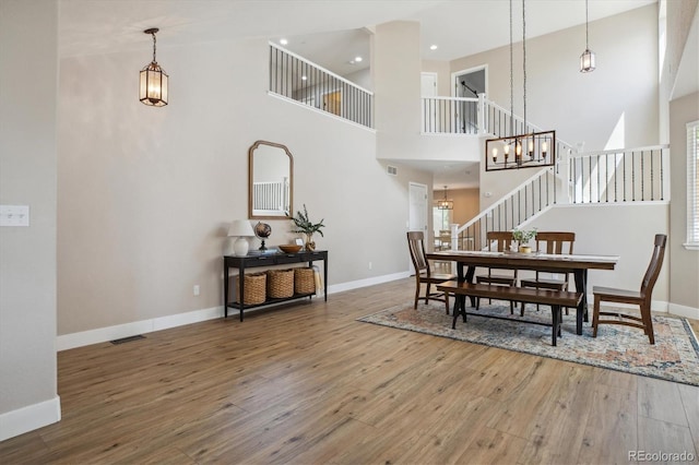 dining area with a towering ceiling, a chandelier, hardwood / wood-style floors, stairway, and baseboards