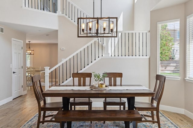dining room featuring a chandelier, plenty of natural light, light wood-style flooring, stairway, and a high ceiling