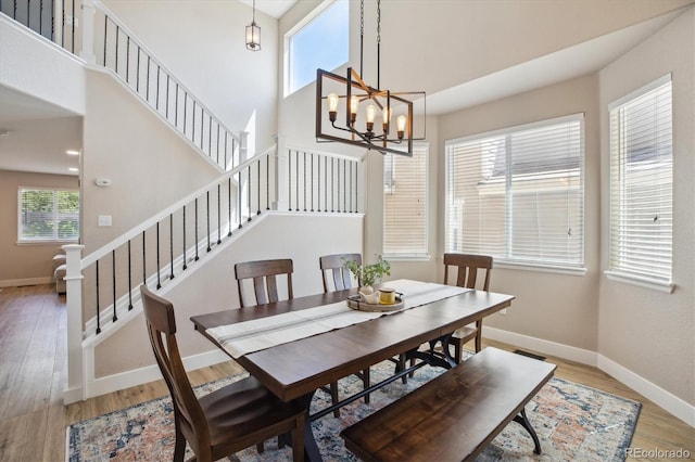 dining room featuring light wood finished floors, baseboards, a towering ceiling, stairs, and a chandelier