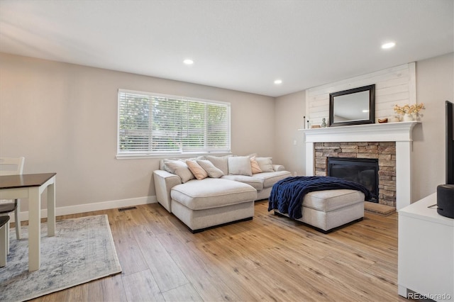 living room featuring a stone fireplace, light wood finished floors, baseboards, and recessed lighting