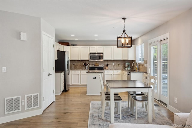 kitchen featuring stainless steel appliances, a sink, decorative backsplash, white cabinets, and light wood finished floors