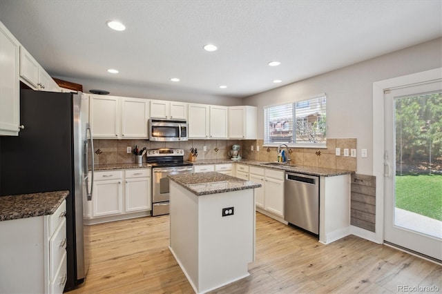 kitchen featuring stainless steel appliances, a center island, light wood-style flooring, white cabinets, and dark stone countertops