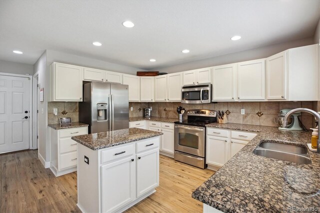 kitchen featuring stainless steel appliances, a sink, dark stone countertops, a center island, and light wood-style floors