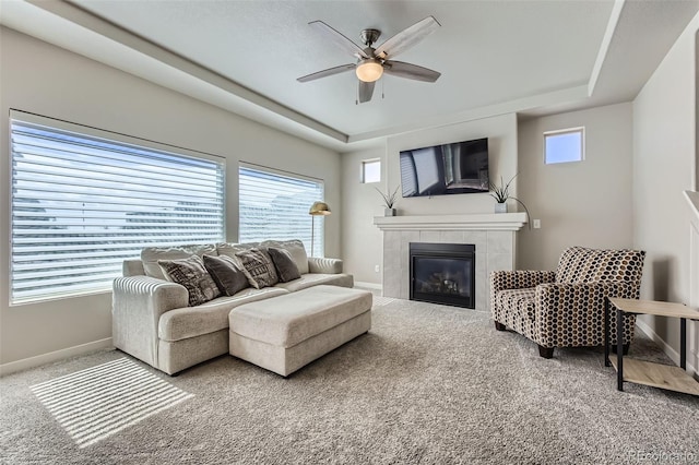 carpeted living room with baseboards, a raised ceiling, a tiled fireplace, and ceiling fan