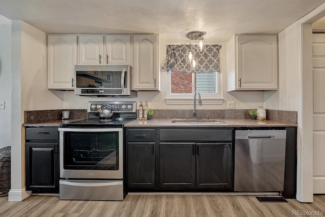 1572 W Long Ave, Littleton, CO 80120 - kitchen featuring appliances with stainless steel finishes, light wood finished floors, white cabinets, a textured ceiling, and dark cabinets