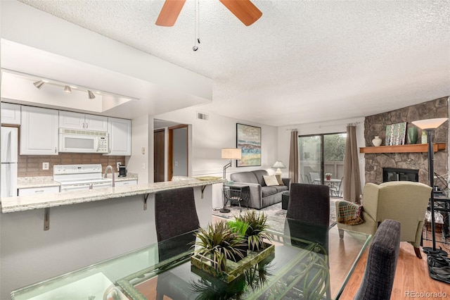 7750 W 87th Dr Unit C, Arvada, CO 80005 - dining space with a textured ceiling, light wood-type flooring, a ceiling fan, and a stone fireplace