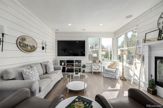 living room with recessed lighting, wooden walls, a brick fireplace, and wood finished floors