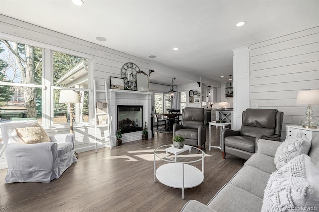 living room featuring a glass covered fireplace, wood walls, and wood finished floors