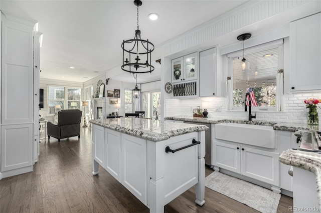 kitchen featuring a healthy amount of sunlight, dark wood-style floors, a kitchen island, a sink, and white cabinets