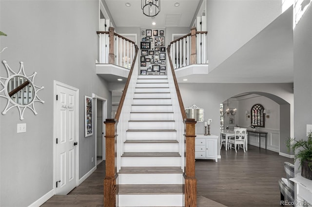 stairs featuring baseboards, a chandelier, a towering ceiling, wood finished floors, and arched walkways