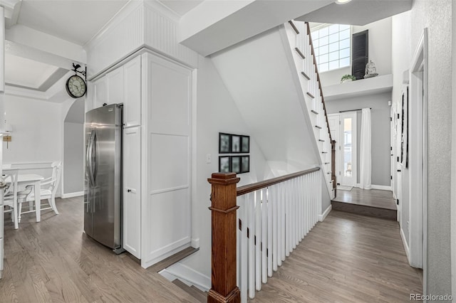 hall with baseboards, arched walkways, a high ceiling, and light wood finished floors