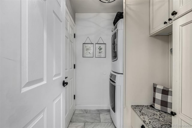 clothes washing area featuring cabinet space, stacked washing maching and dryer, marble finish floor, and baseboards