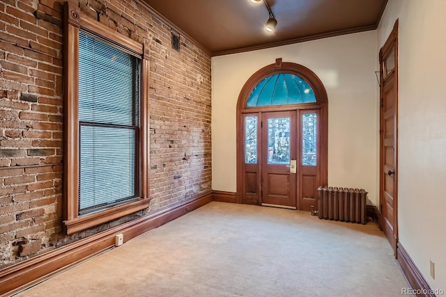 carpeted entrance foyer with rail lighting, crown molding, radiator heating unit, and brick wall