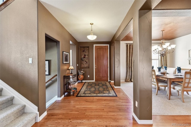 foyer entrance featuring stairs, baseboards, light wood finished floors, and an inviting chandelier