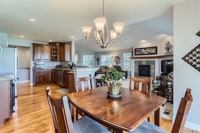 dining space with a fireplace, ceiling fan with notable chandelier, baseboards, lofted ceiling, and light wood-type flooring
