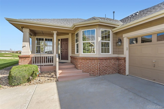 entrance to property featuring a porch, driveway, roof with shingles, a garage, and brick siding