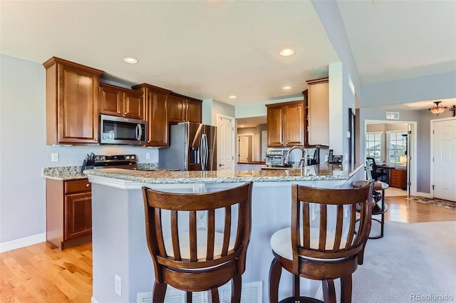 kitchen with appliances with stainless steel finishes, light stone countertops, a breakfast bar, and a peninsula
