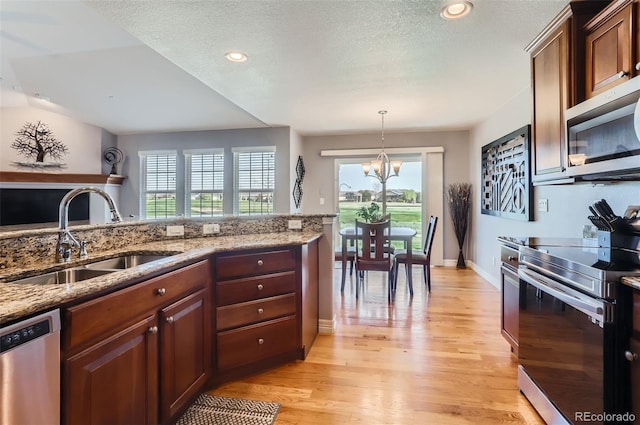 kitchen with appliances with stainless steel finishes, an inviting chandelier, a sink, light wood finished floors, and a wealth of natural light