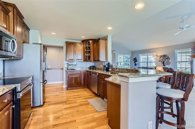 kitchen with appliances with stainless steel finishes, a breakfast bar, light wood-style flooring, a peninsula, and lofted ceiling
