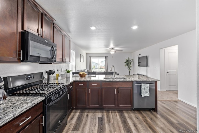 kitchen with a peninsula, ceiling fan, a sink, light wood finished floors, and black appliances