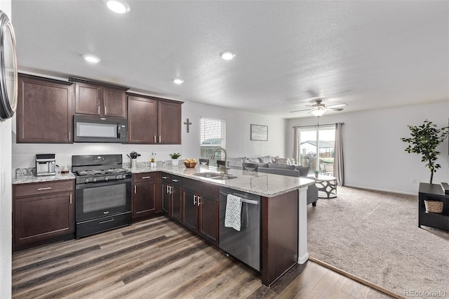 kitchen featuring dark brown cabinetry, a sink, a peninsula, open floor plan, and black appliances