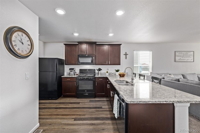 kitchen with dark brown cabinetry, a sink, a peninsula, dark wood-type flooring, and black appliances