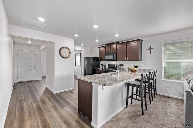 kitchen with visible vents, dark brown cabinets, baseboards, black appliances, and a breakfast bar