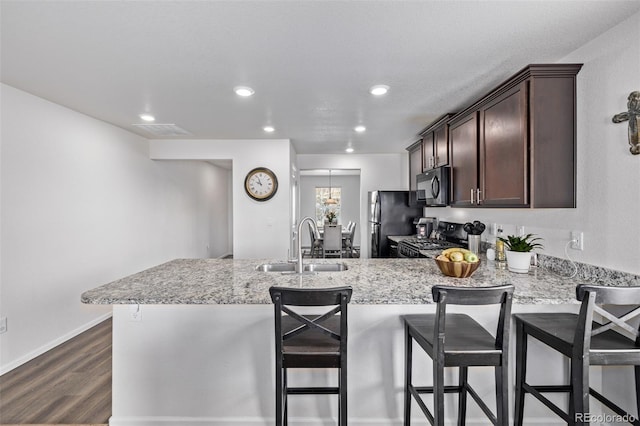 kitchen with visible vents, a peninsula, dark brown cabinetry, a sink, and black appliances