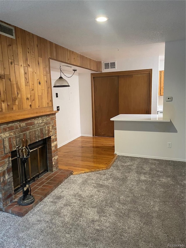 unfurnished living room featuring dark colored carpet, a brick fireplace, and wood walls