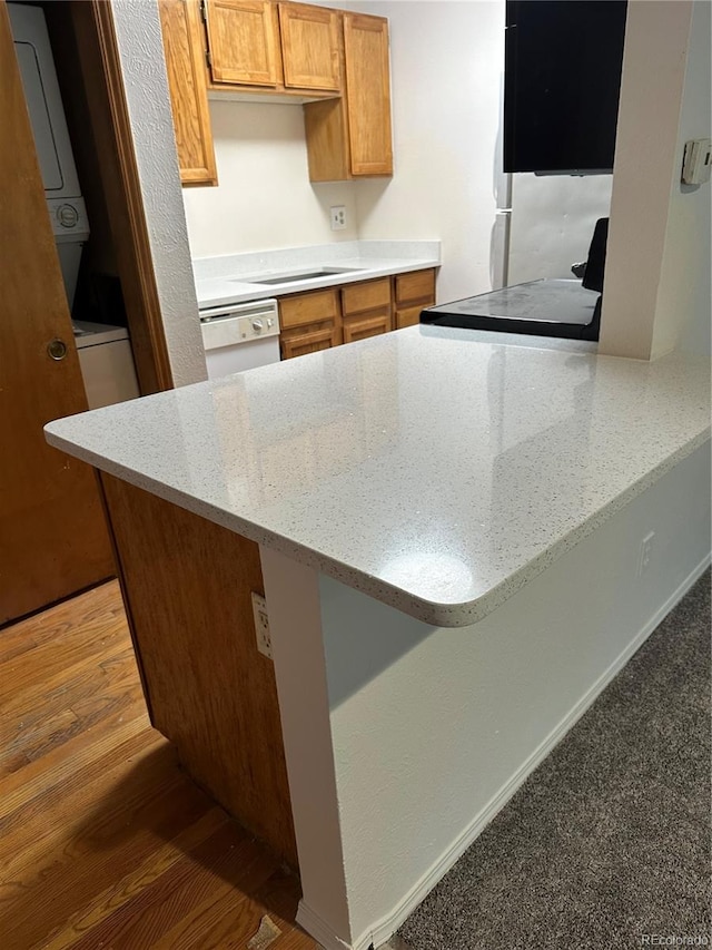 kitchen featuring stacked washer and dryer, dishwasher, and kitchen peninsula